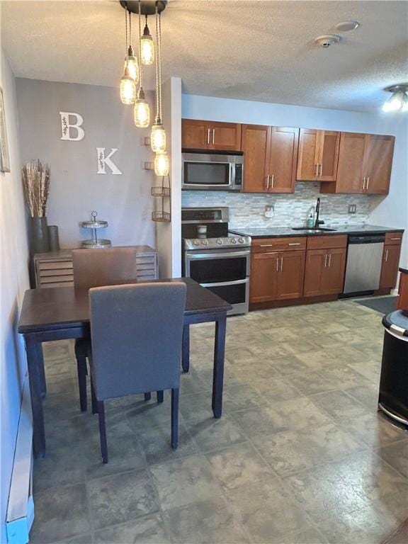 kitchen with a textured ceiling, decorative light fixtures, tasteful backsplash, a sink, and stainless steel appliances