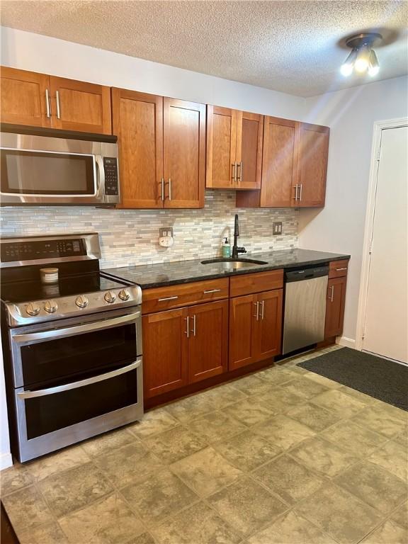 kitchen with appliances with stainless steel finishes, a sink, a textured ceiling, brown cabinetry, and tasteful backsplash