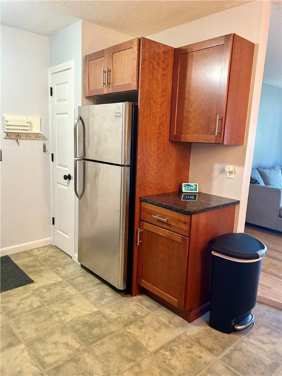 kitchen featuring dark countertops, brown cabinetry, freestanding refrigerator, and a textured ceiling