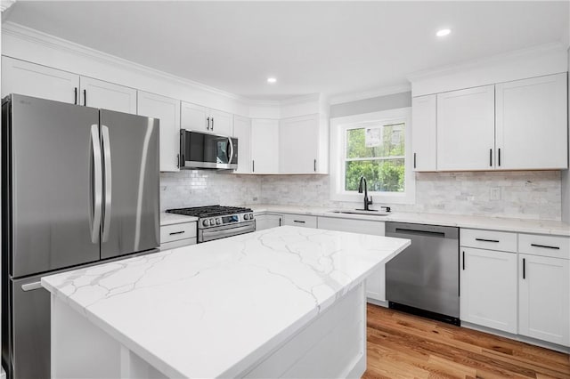 kitchen featuring crown molding, appliances with stainless steel finishes, a sink, white cabinets, and light wood finished floors