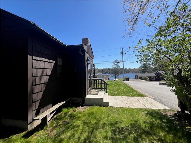 view of side of property with a yard, a water view, and a chimney