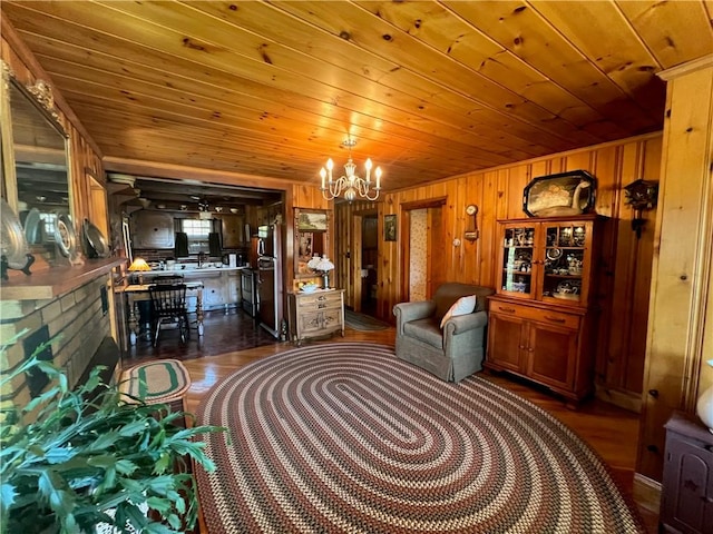 living area with wooden walls, a notable chandelier, dark wood-style floors, and wood ceiling