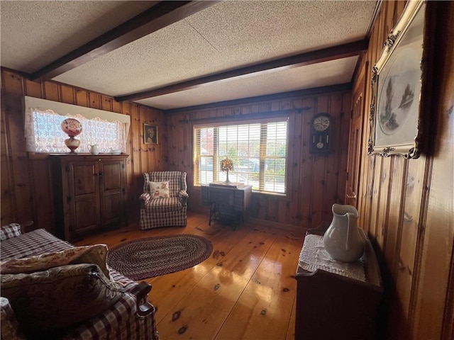 living area with wooden walls, a textured ceiling, beam ceiling, and light wood-type flooring