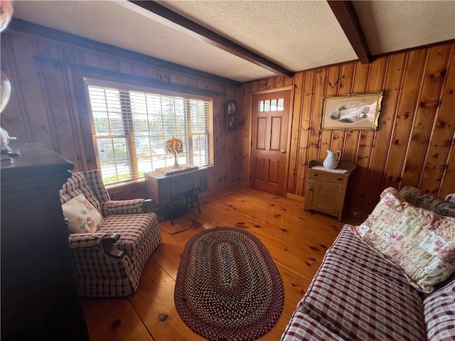 interior space featuring wooden walls, a textured ceiling, beamed ceiling, and light wood finished floors
