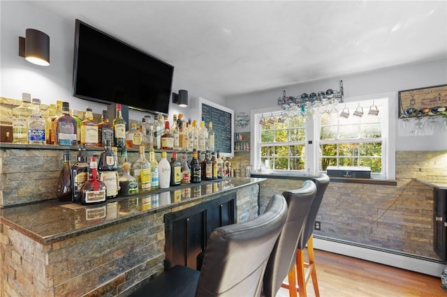 bar with a dry bar, backsplash, wood finished floors, and baseboard heating
