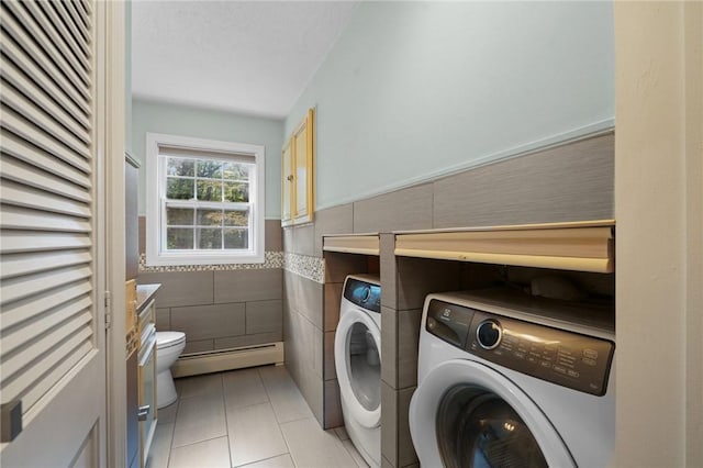 washroom with washing machine and clothes dryer, tile walls, baseboard heating, a wainscoted wall, and light tile patterned flooring