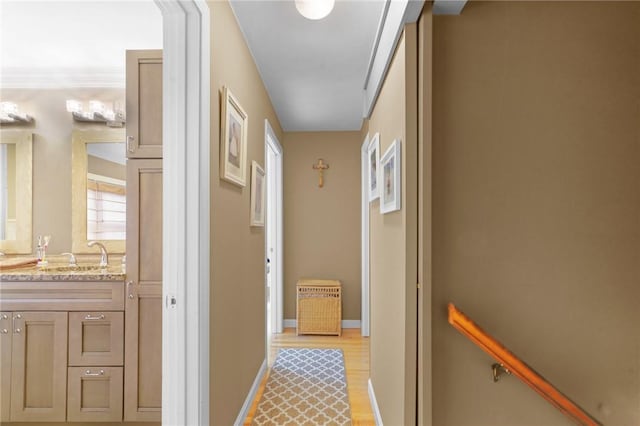 corridor featuring light wood-type flooring, a sink, and baseboards