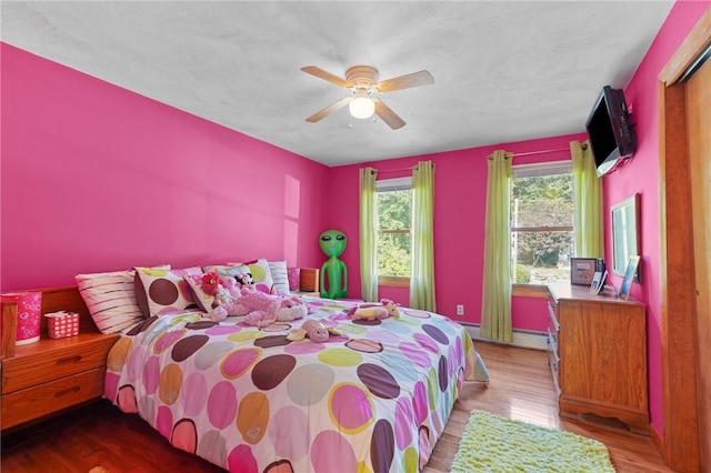 bedroom featuring a ceiling fan, baseboard heating, and light wood-type flooring