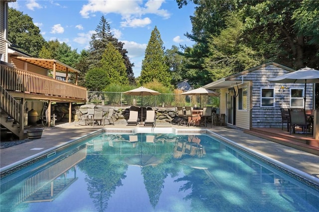 pool featuring outdoor dining space, a wooden deck, stairway, an outbuilding, and a patio