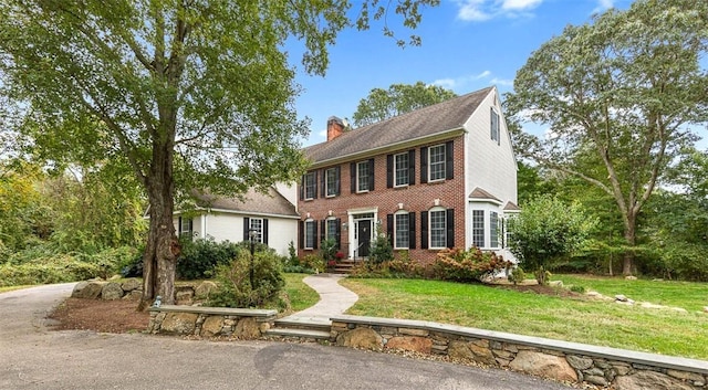 colonial inspired home with brick siding, a front lawn, and a chimney