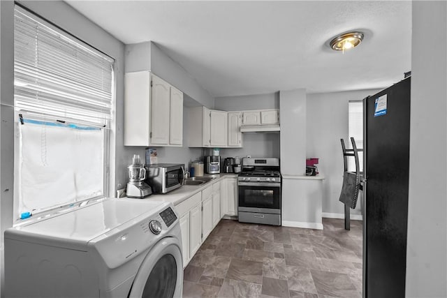 752 Social St, Woonsocket, RI 02895 - kitchen with washer / dryer, a healthy amount of sunlight, white cabinetry, under cabinet range hood, and appliances with stainless steel finishes