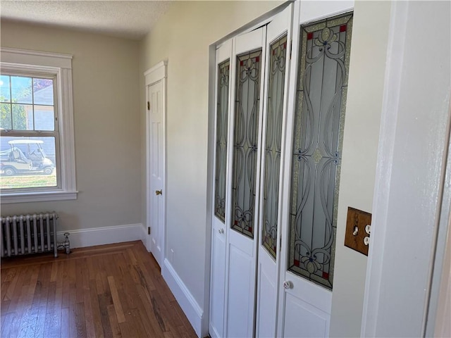 hallway featuring baseboards, dark wood-style floors, and radiator heating unit