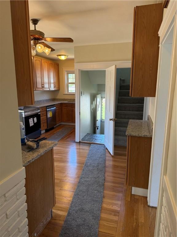 kitchen with brown cabinetry, stainless steel dishwasher, a ceiling fan, and wood finished floors