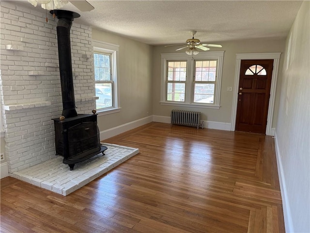 unfurnished living room with a wood stove, ceiling fan, baseboards, and radiator
