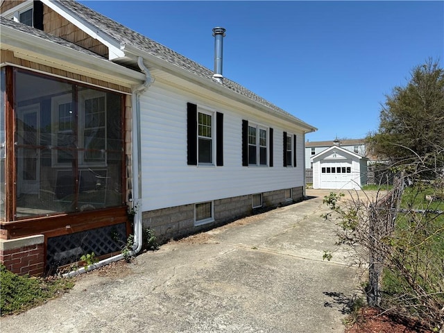 view of side of home with a sunroom, roof with shingles, an outbuilding, and concrete driveway