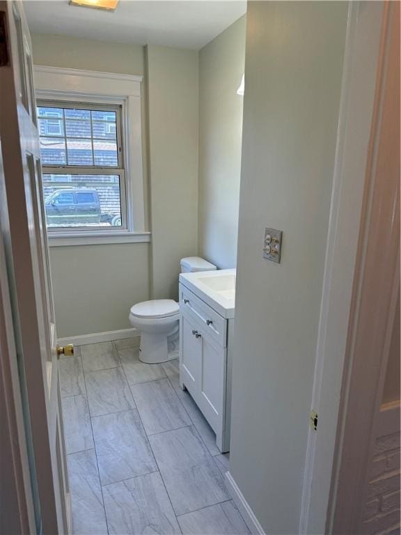 half bath featuring vanity, baseboards, toilet, and marble finish floor