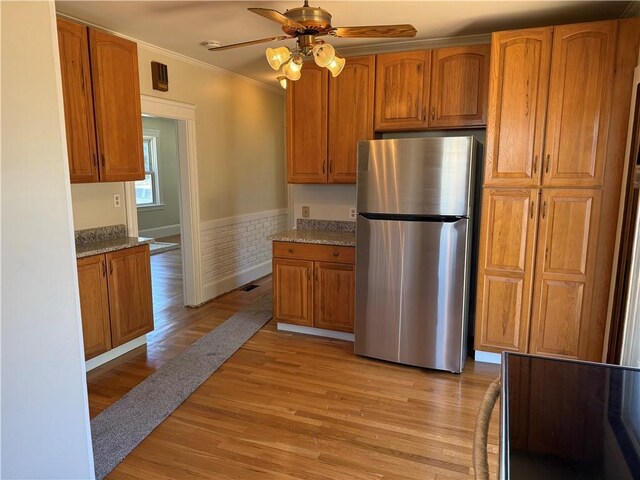 kitchen featuring freestanding refrigerator, crown molding, brown cabinetry, and light wood-type flooring