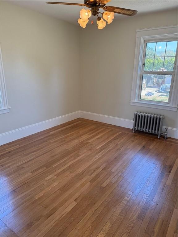 empty room featuring hardwood / wood-style flooring, ceiling fan, baseboards, and radiator