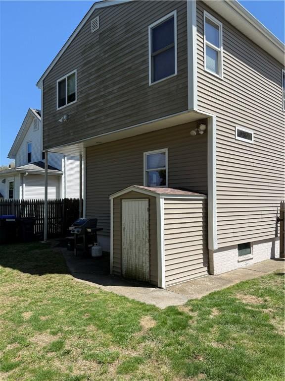 rear view of house featuring a lawn, an outdoor structure, a shed, and fence