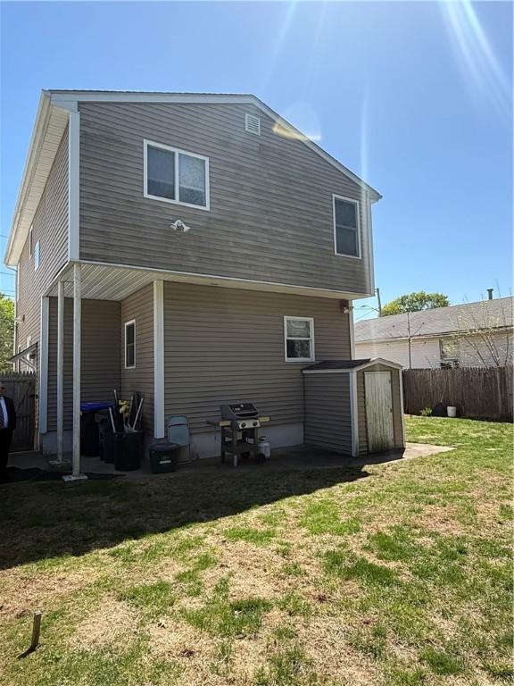 rear view of house featuring a storage shed, fence, an outdoor structure, and a yard