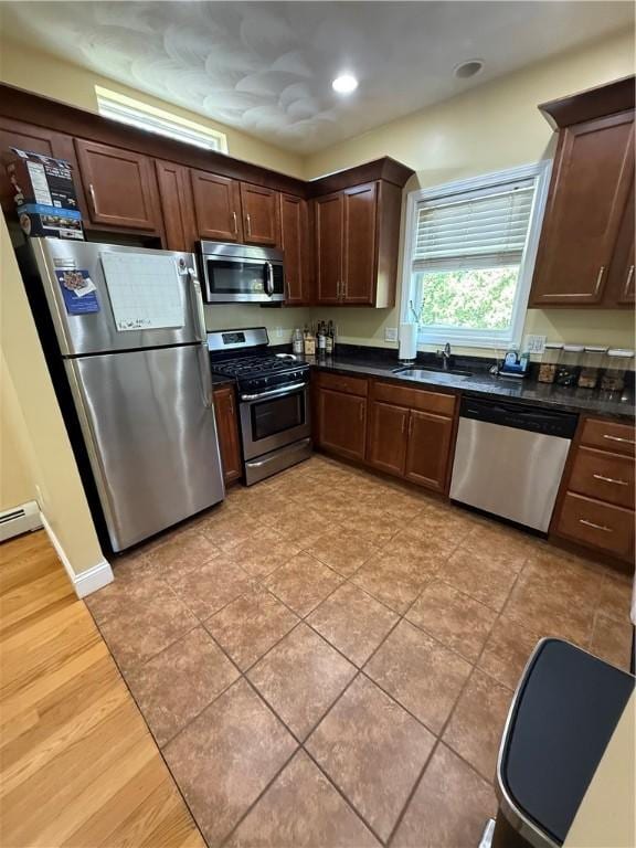 kitchen with a sink, appliances with stainless steel finishes, dark brown cabinetry, and dark countertops