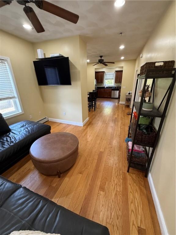 living room featuring a baseboard radiator, baseboards, ceiling fan, and light wood-style floors