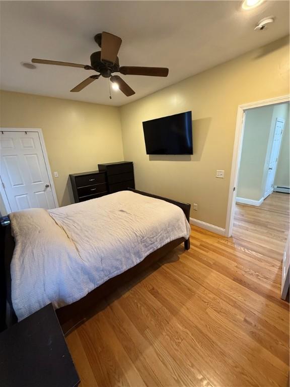 bedroom with baseboards, ceiling fan, a baseboard heating unit, and light wood-type flooring