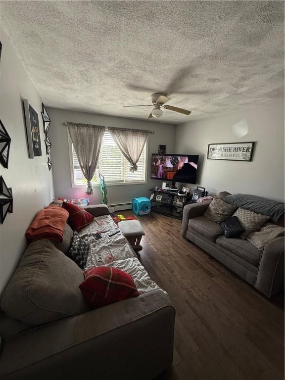 living area with baseboard heating, a textured ceiling, ceiling fan, and wood finished floors