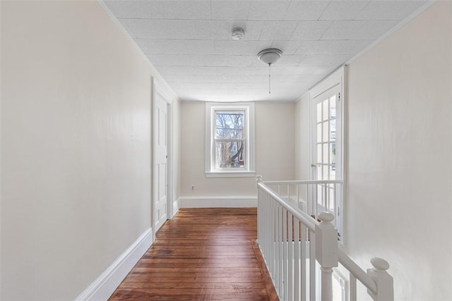 hallway with wood-type flooring, baseboards, crown molding, and an upstairs landing
