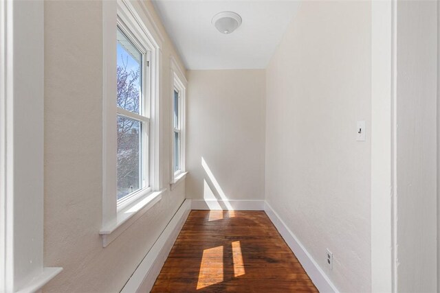corridor featuring baseboards and dark wood-style floors