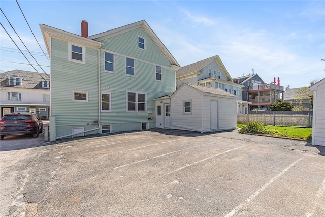 rear view of property featuring fence, uncovered parking, and a chimney