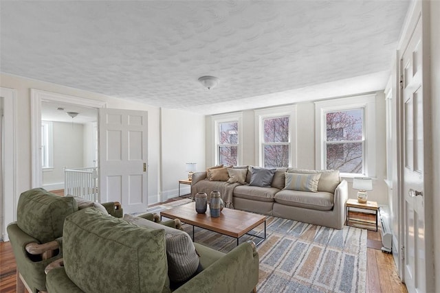 living area featuring baseboards, plenty of natural light, light wood finished floors, and a textured ceiling