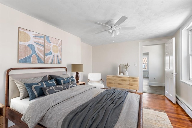 bedroom featuring a ceiling fan, baseboards, wood finished floors, and a baseboard radiator