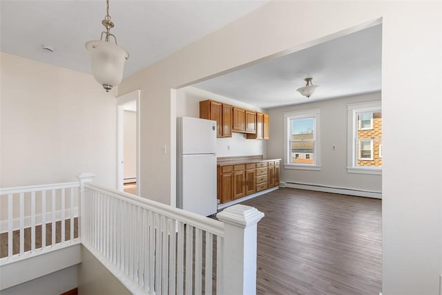 kitchen with freestanding refrigerator, pendant lighting, baseboard heating, dark wood-style floors, and brown cabinets