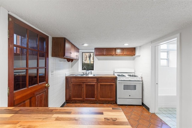 kitchen featuring white gas range oven, a sink, a textured ceiling, and dark tile patterned flooring