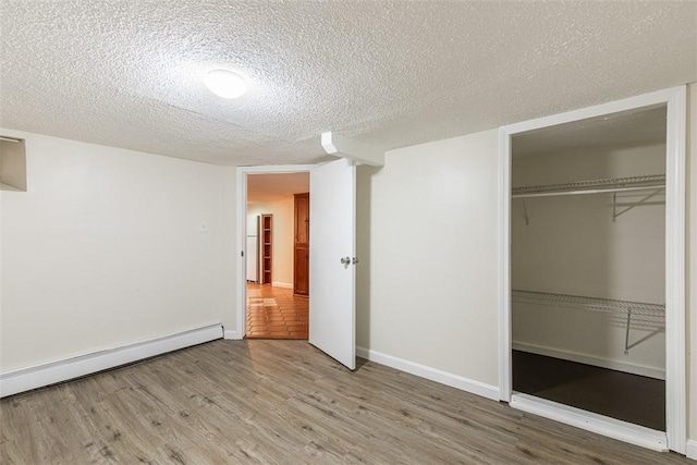 unfurnished bedroom featuring baseboard heating, a closet, a textured ceiling, and wood finished floors