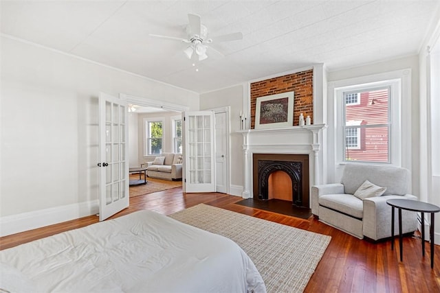 bedroom featuring a fireplace with flush hearth, crown molding, wood-type flooring, and french doors