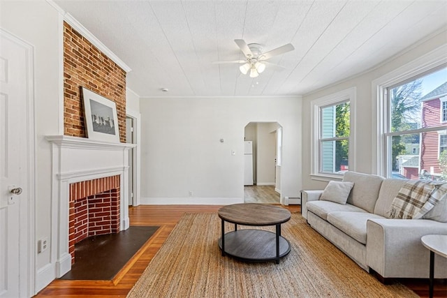 living area featuring crown molding, baseboard heating, arched walkways, a fireplace with flush hearth, and wood finished floors