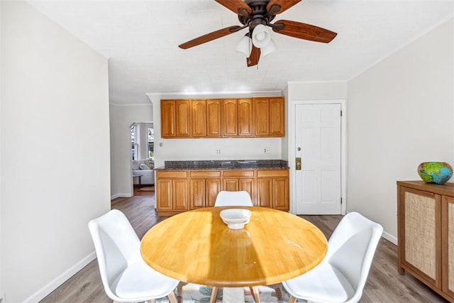 dining space with crown molding, a ceiling fan, baseboards, and light wood-style flooring