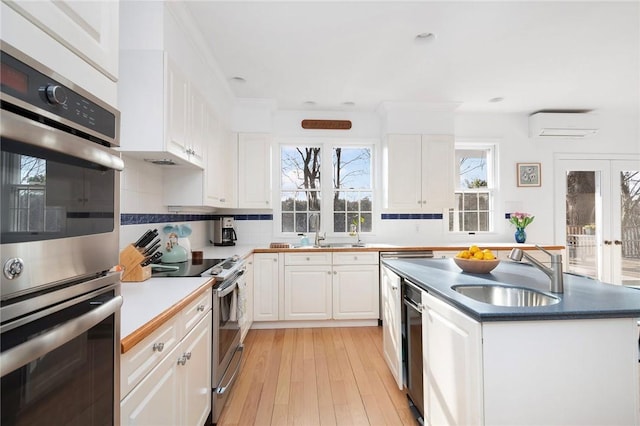 kitchen featuring a wall mounted air conditioner, a center island, white cabinetry, a sink, and stainless steel appliances