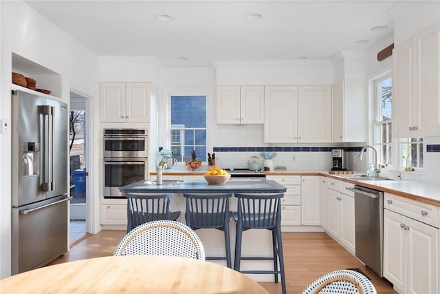 kitchen featuring white cabinets, a sink, light wood finished floors, stainless steel appliances, and decorative backsplash