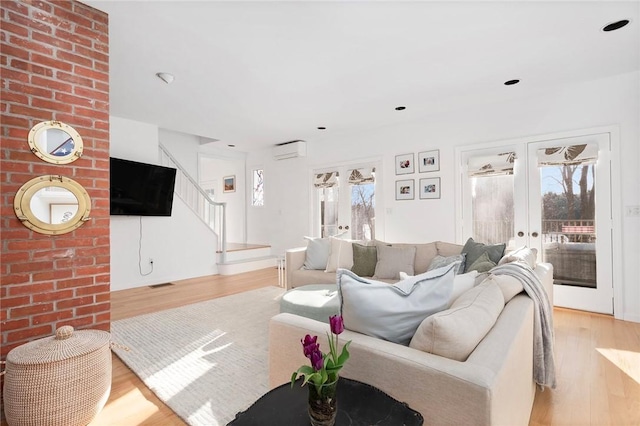 living room featuring light wood-style flooring, a wall unit AC, french doors, and stairway