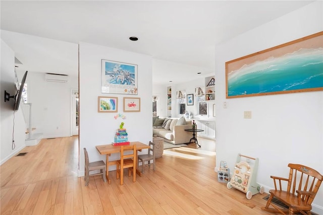 interior space with a wall mounted AC, light wood-type flooring, and visible vents