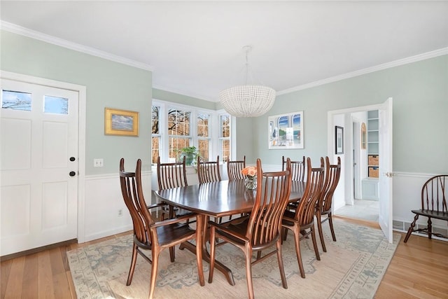 dining space with ornamental molding, light wood-style flooring, and a notable chandelier