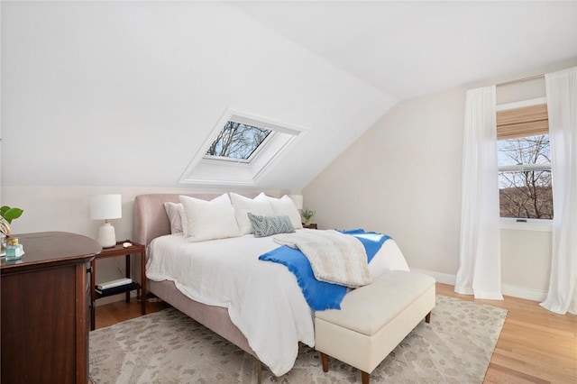 bedroom with baseboards, light wood-style flooring, and vaulted ceiling with skylight