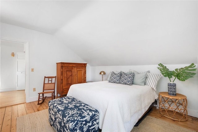 bedroom with baseboards, vaulted ceiling, and light wood-style flooring
