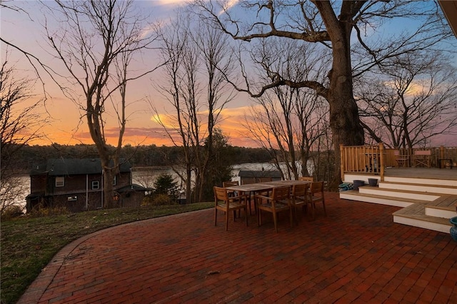 patio terrace at dusk with a deck with water view and outdoor dining area