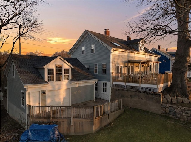 back of property at dusk featuring a shingled roof and a deck