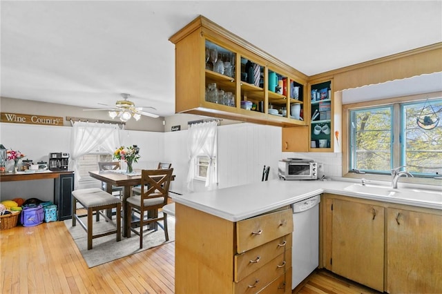 kitchen with white dishwasher, a sink, light countertops, a ceiling fan, and light wood-type flooring