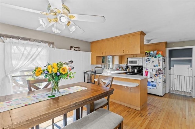 kitchen featuring a sink, white appliances, light countertops, light wood-style flooring, and a peninsula